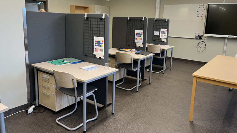 Skolbänkar på rad med avskärmningar vid varje bord.